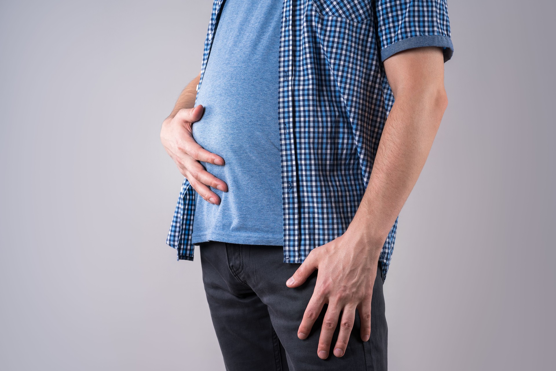 Hombre gordo con hinchazón y dolor abdominal, sobrepeso cuerpo masculino sobre fondo gris