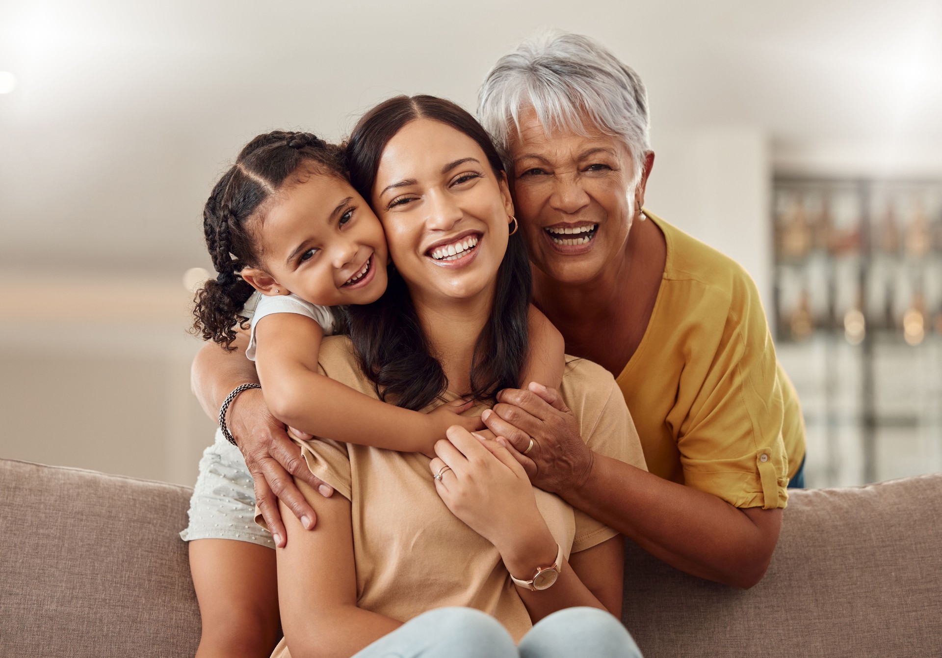 Abuela, mamá e hijo se abrazan en un retrato para el día de las madres en el sofá de una casa como una familia feliz en Colombia. Sonríe, a mamá y a la anciana les encanta abrazar a una niña o niño y disfrutar de tiempo de calidad