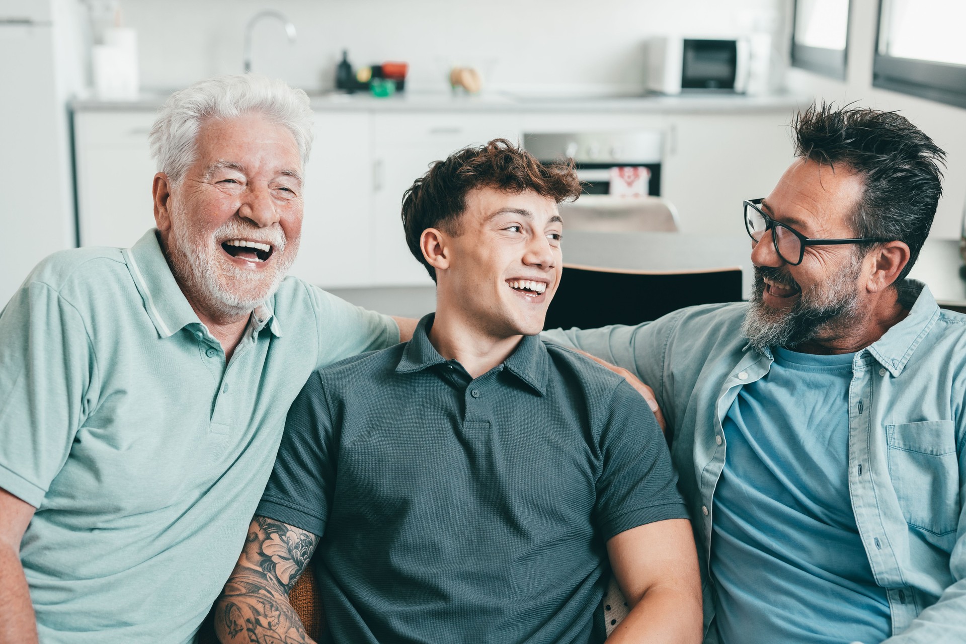 La feliz familia multigeneracional de hombres se mantiene unida con diversión. Abuelo, hijo maduro y nieto joven riendo mientras están sentados en el sofá de casa